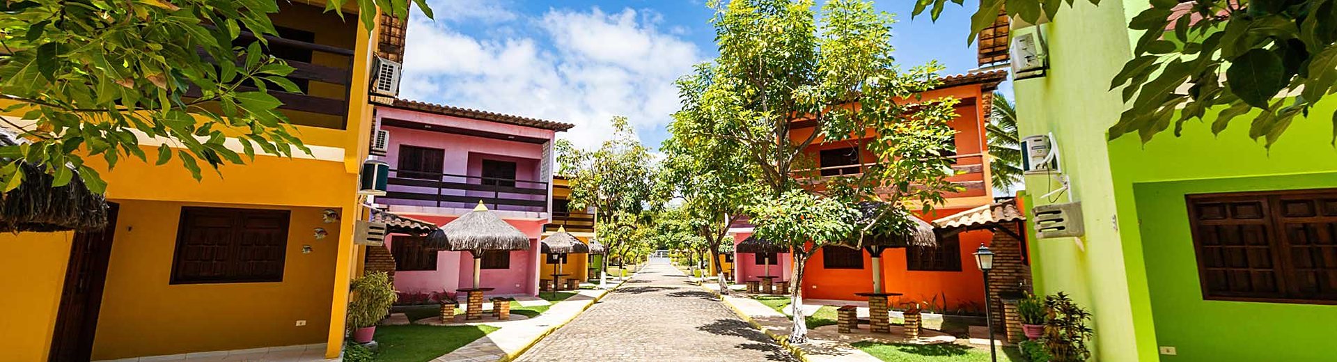 Alameda da pousada com os chalés coloridos e os quiosques de palha