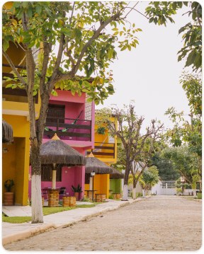 Alameda da pousada com os chalés coloridos e quiosques de palha