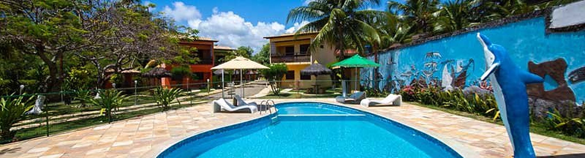 Piscina ao ar livre com espreguiçadeiras cercada por coqueiros