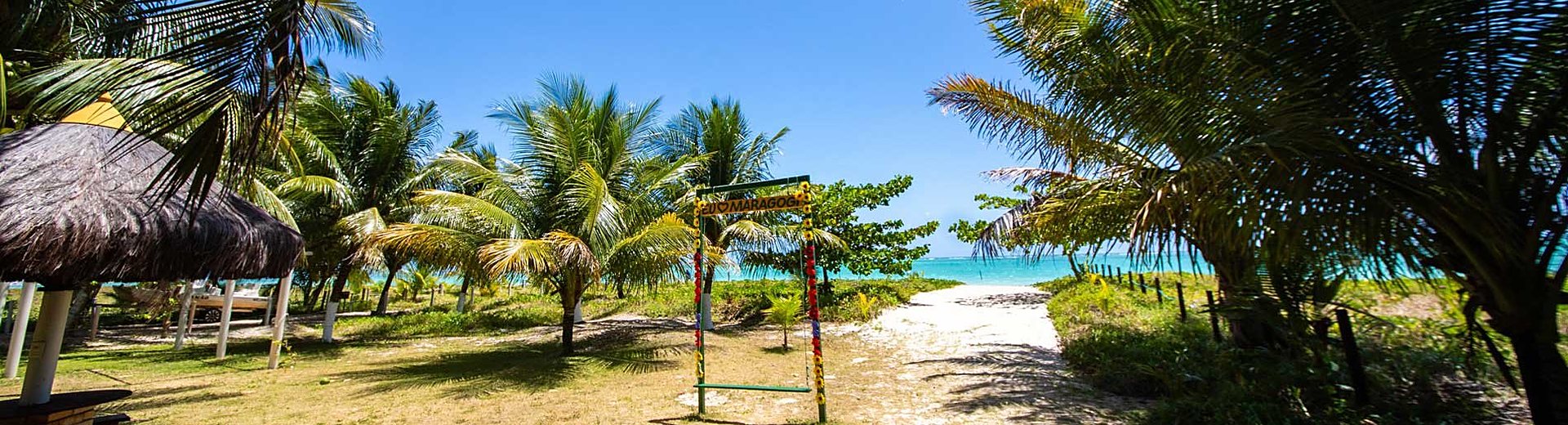 Faixa de areia e mar de águas claras com a vila ao fundo