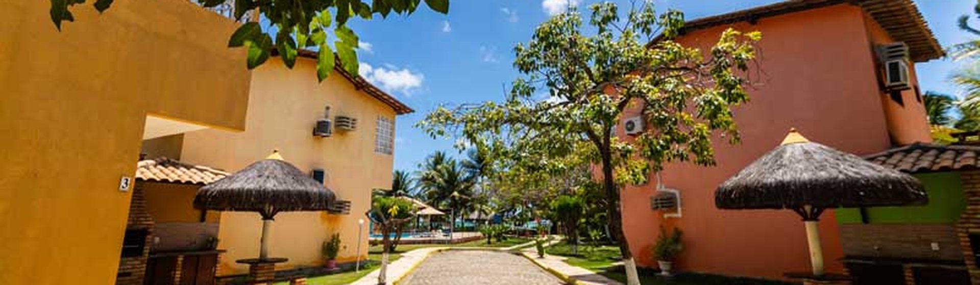 Alameda da pousada com chalés coloridos e quiosques de palha
