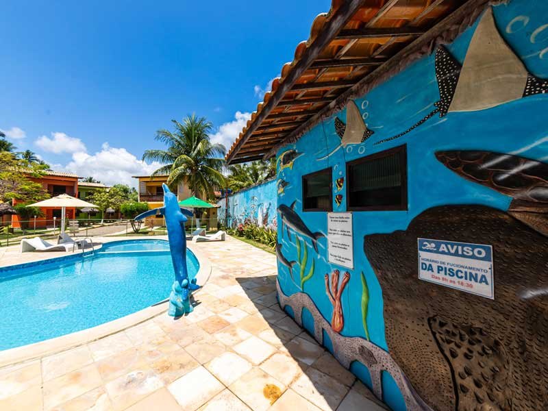 Piscina com a escultura de golfinho e os chalés ao fundo